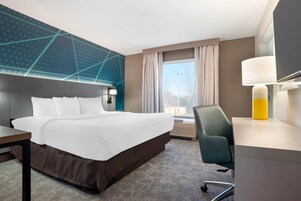 A hotel room with a large bed, a desk, a chair, a window with curtains, and a wall with a geometric pattern.