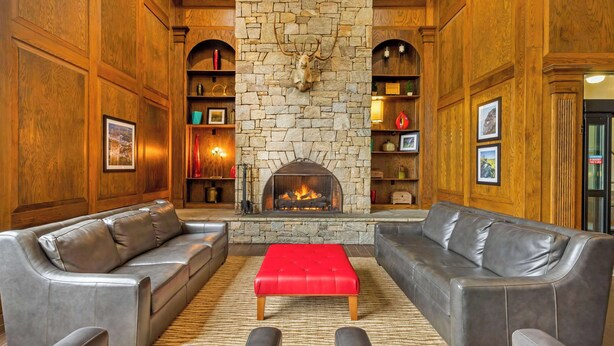 A cozy living room with a stone fireplace, leather sofas, and a red ottoman. - Comfort Suites Boone - University Area (Boone)
