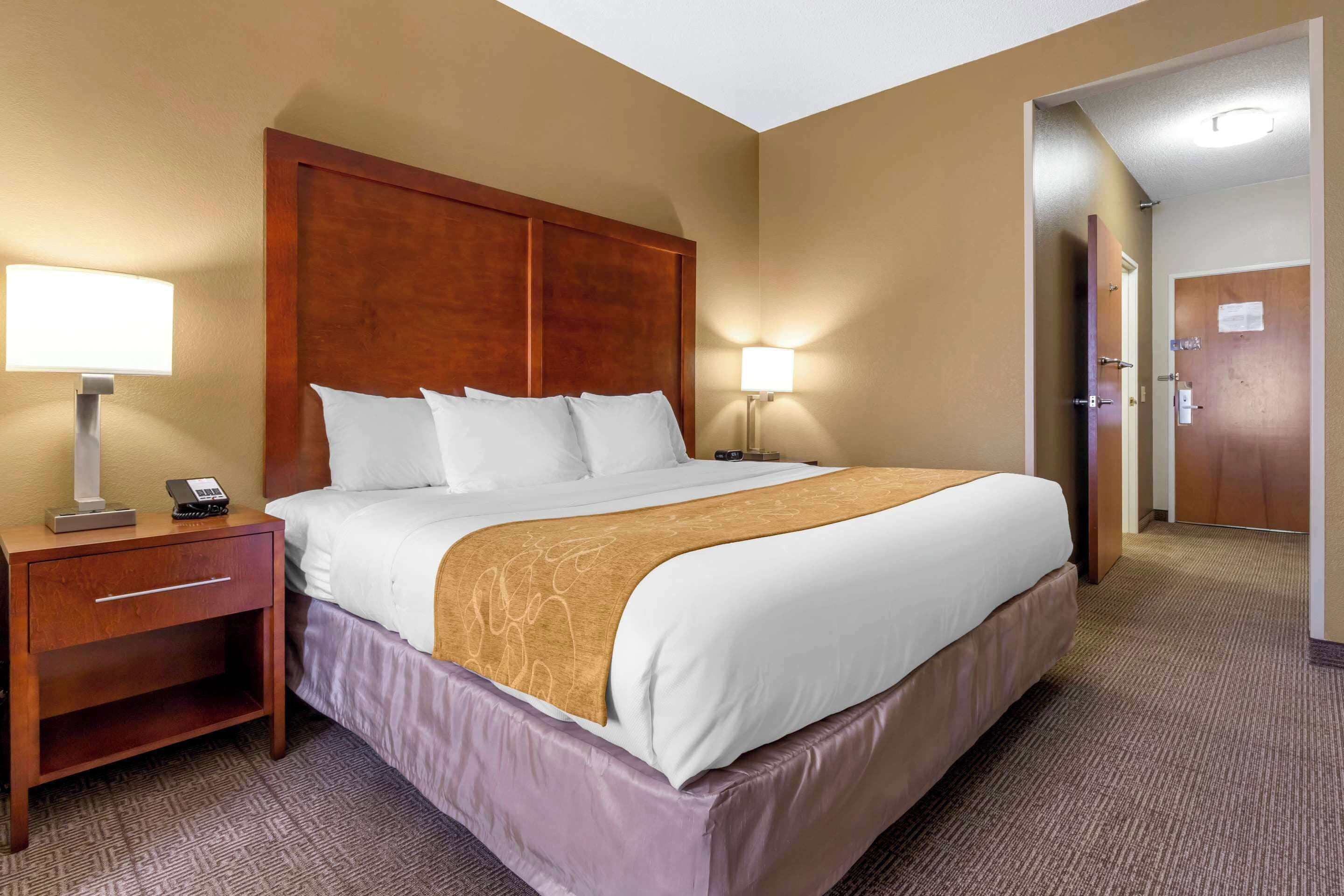 A hotel room with a large bed, two bedside lamps, a wooden nightstand, and a door to the bathroom.