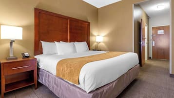 A hotel room with a large bed, two bedside lamps, a wooden nightstand, and a door to the bathroom.