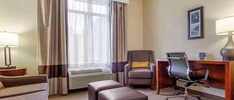 A hotel room with a sofa, a desk, an office chair, a lamp, and a picture on the wall.