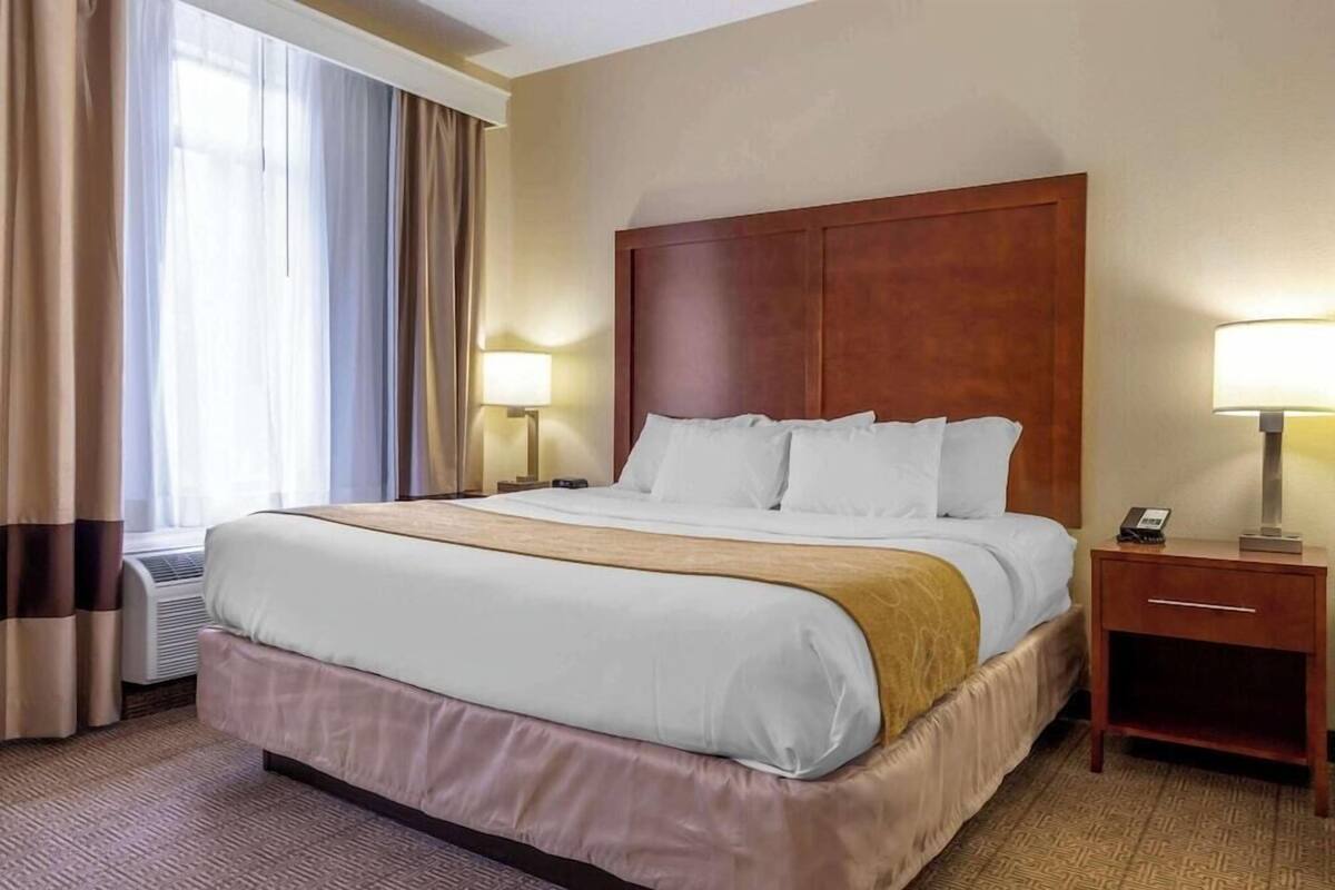 Ein Hotelzimmer mit einem großen Bett, Nachttischen, einer Lampe und einem Fenster mit Vorhängen.