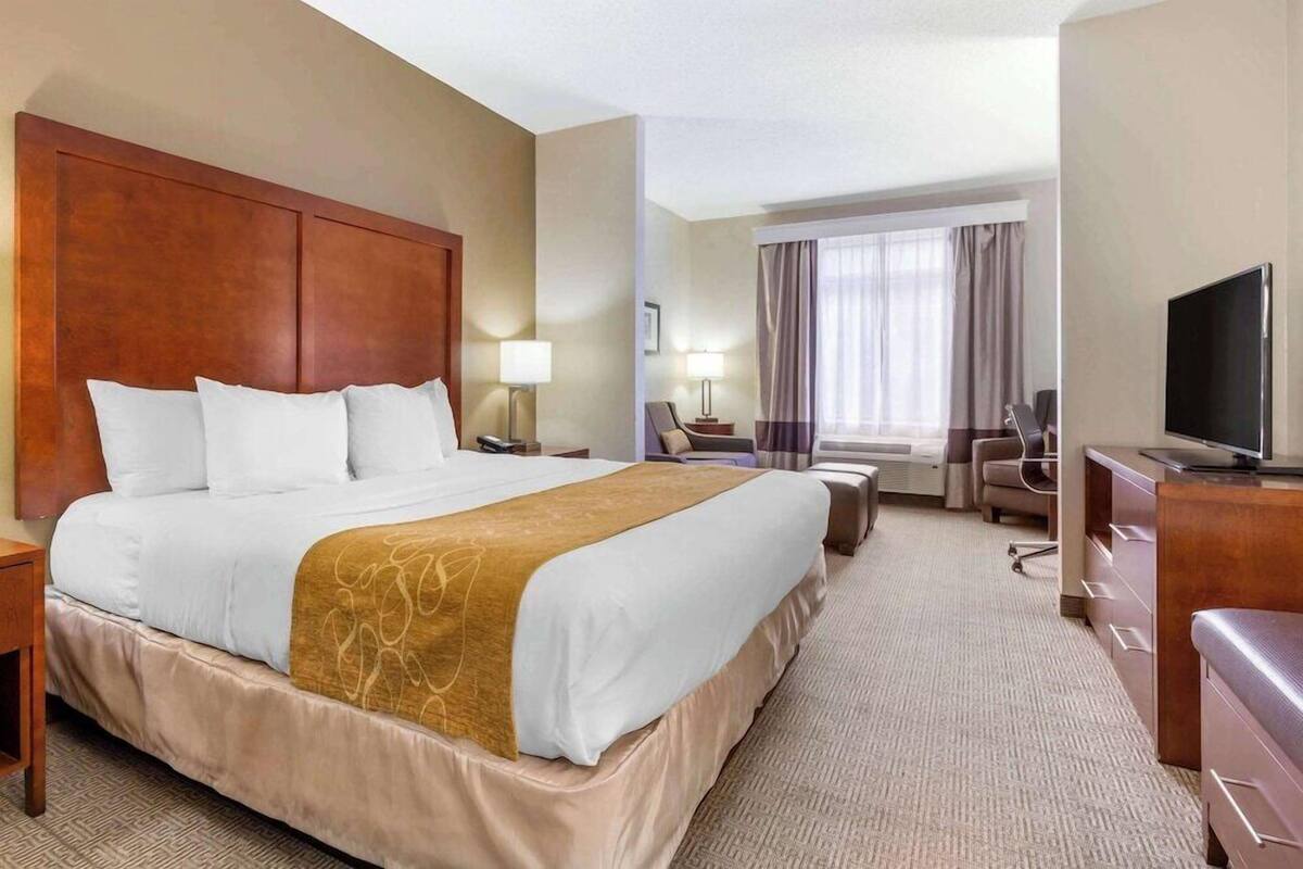Ein Hotelzimmer mit einem großen Bett, einem Schreibtisch, einem Fernseher und einem Fenster mit Vorhängen.
