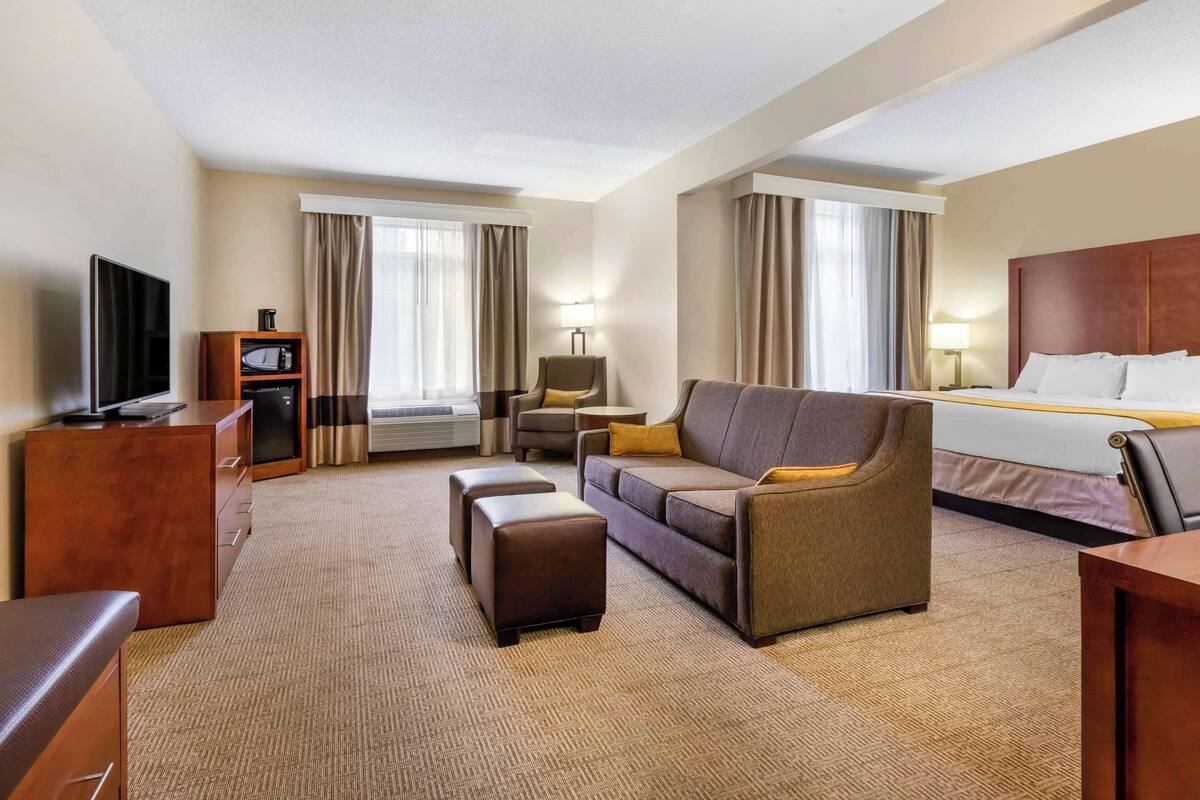 Ein Hotelzimmer mit einem Bett, einem Sofa, einem Fernseher, einem Schreibtisch und einer Lampe.