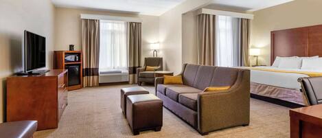 A hotel room with a bed, a sofa, a TV, a desk, and a lamp.