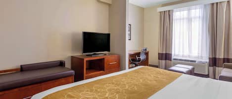 Une chambre d’hôtel avec un lit, un téléviseur posé sur un meuble en bois, un coin salon avec un banc et une fenêtre avec des rideaux.