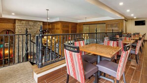 A restaurant with wooden tables and striped chairs, a stone wall, and a staircase with a wrought iron railing. - Comfort Suites Boone - University Area (Boone)