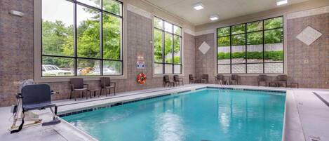 A large indoor swimming pool with clear windows, chairs, and a lifebuoy.