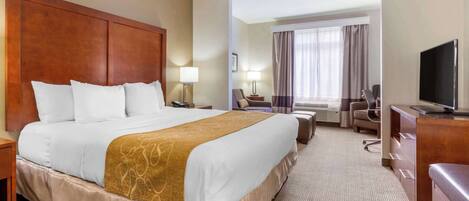A hotel room with a large bed, a desk, a television, and a window with curtains.