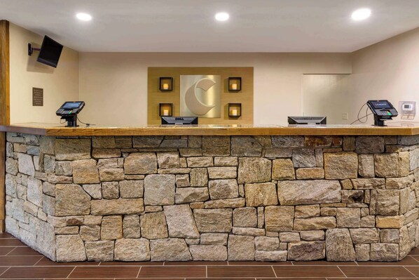 Una recepción con fachada de piedra, un gran letrero iluminado con la letra 'C' y un televisor de pantalla plana montado en la pared.