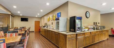 A hotel dining area with wooden tables and chairs, a buffet counter, and a clock on the wall.