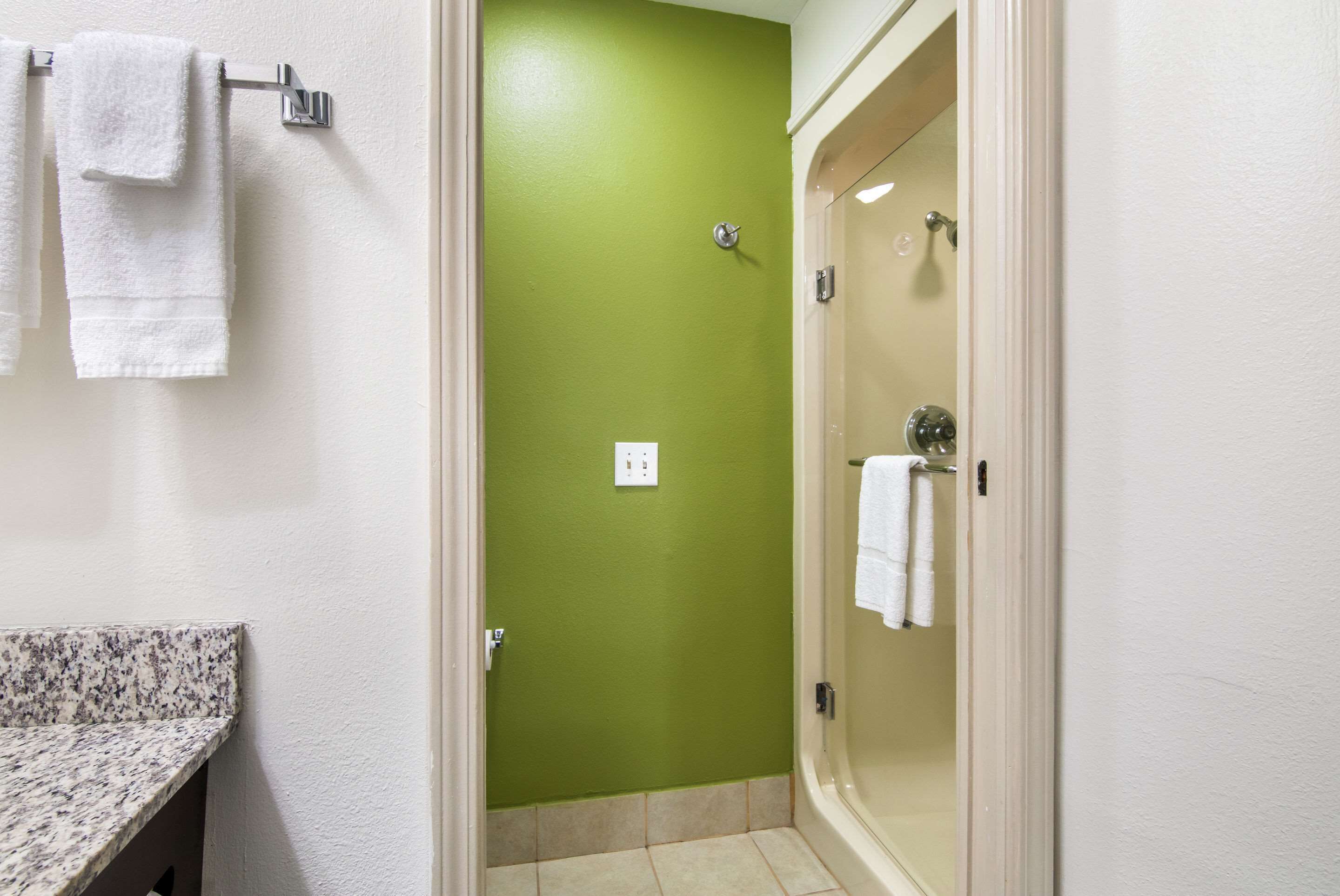 A bathroom with a green wall, a white sink, and a glass-enclosed shower.