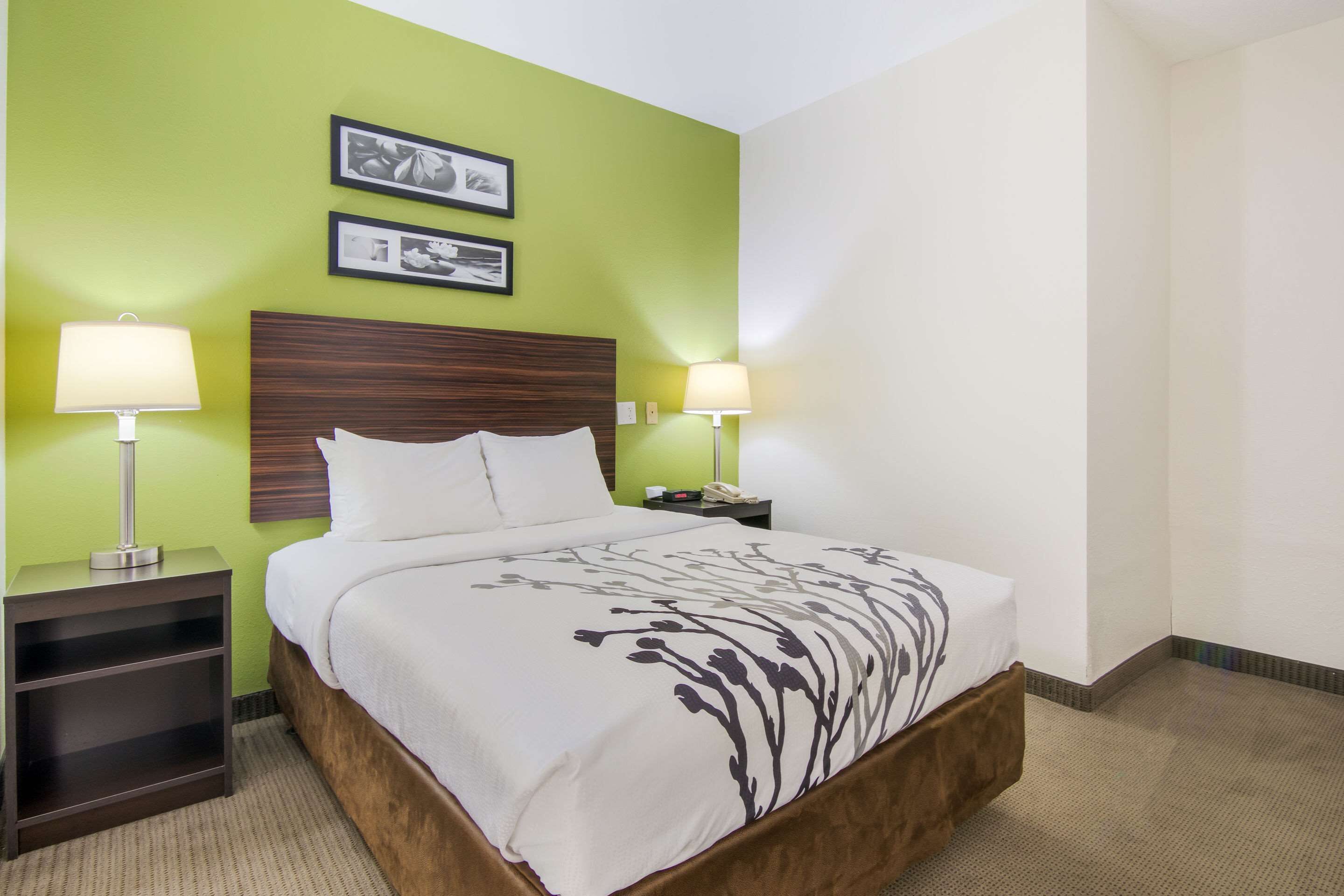 A hotel room with a bed, two bedside lamps, a nightstand, and two framed pictures on the wall.