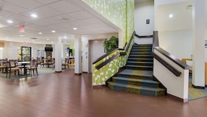 A spacious lobby with a staircase, multiple seating areas, and a large plant.