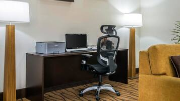 A hotel room with a desk, a computer, a printer, a black office chair, a yellow armchair, and two standing lamps.