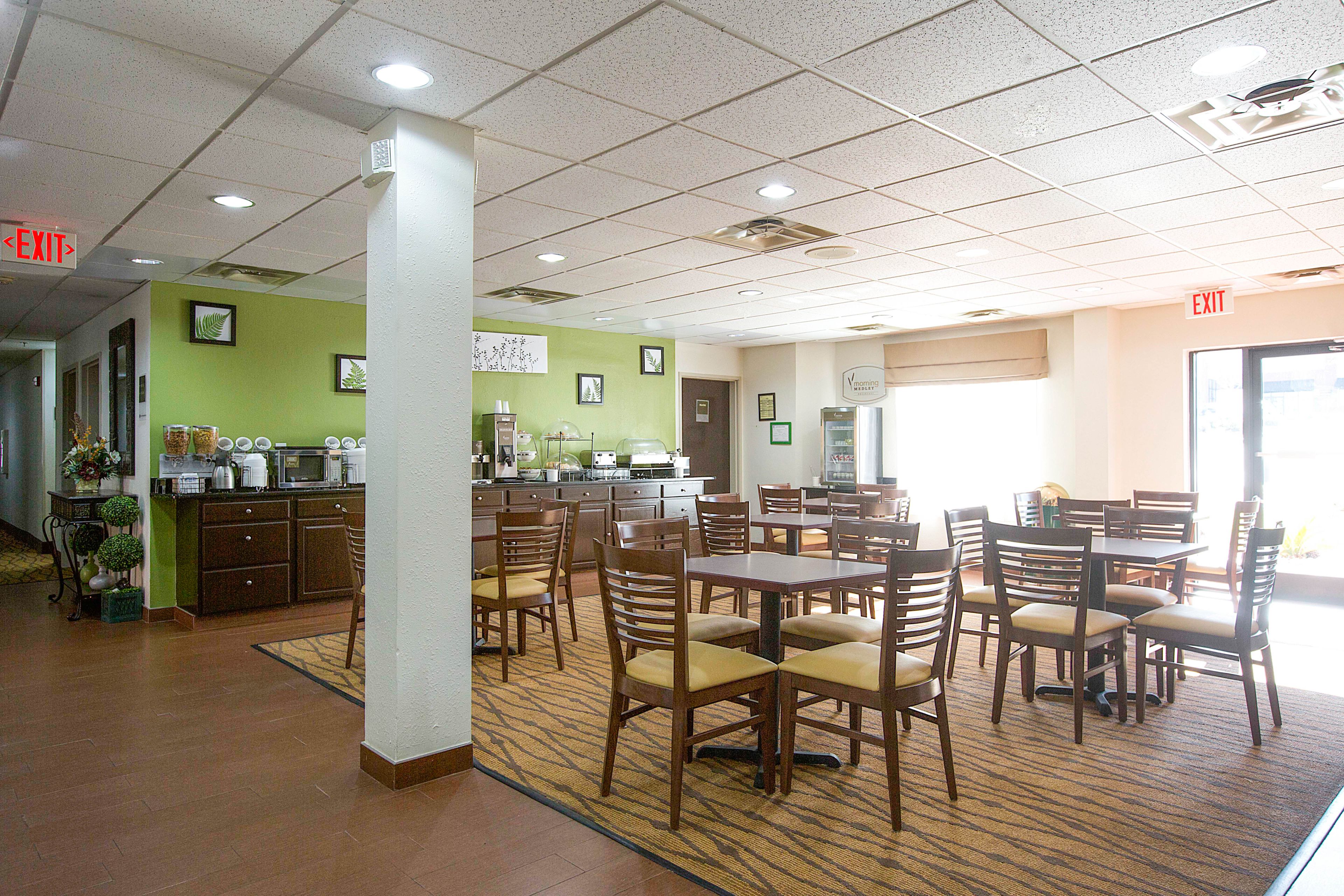 A dining area with multiple tables and chairs, a kitchen area with appliances, and an exit sign.