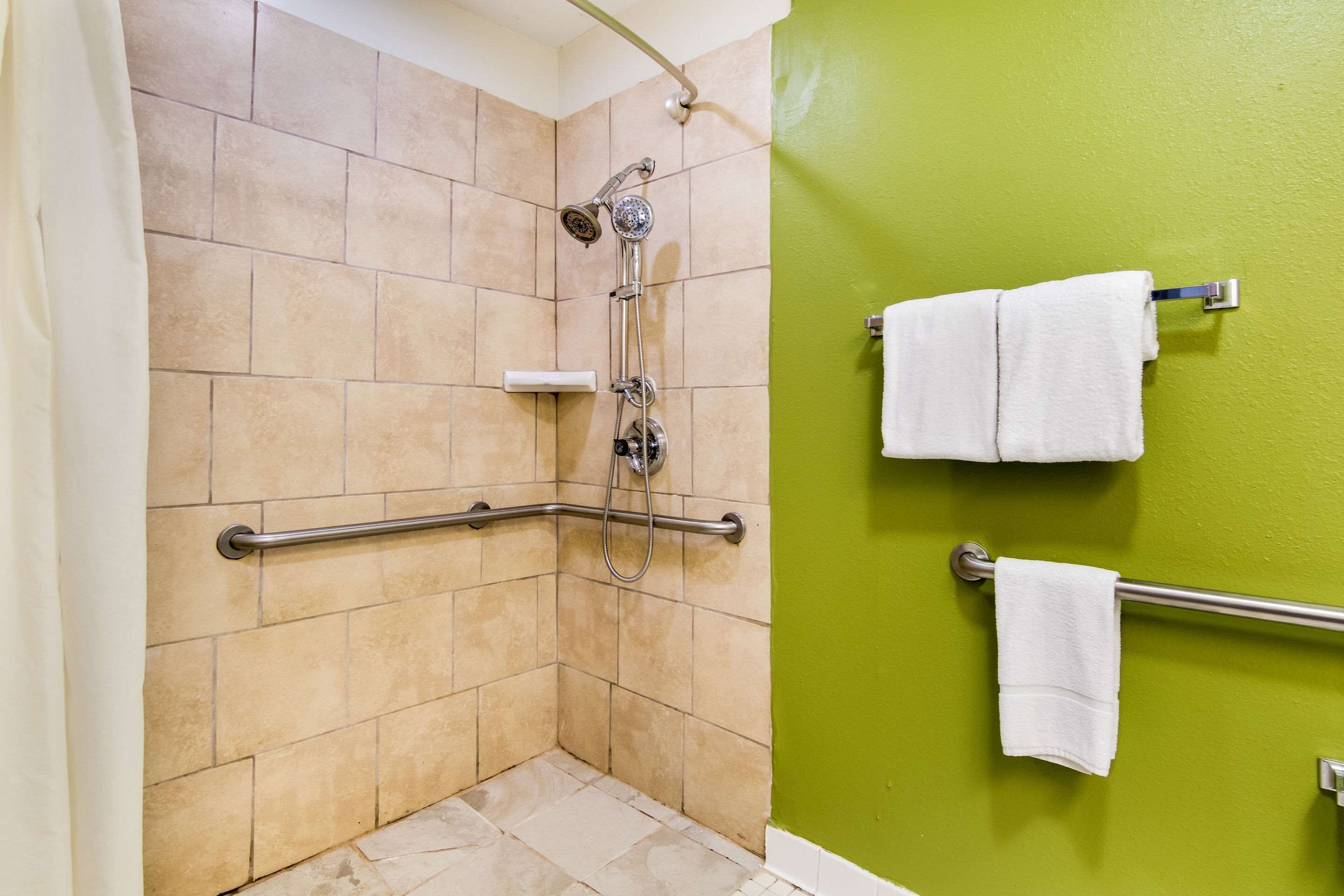A shower with a handheld showerhead, a handheld shower attachment, and a grab bar.