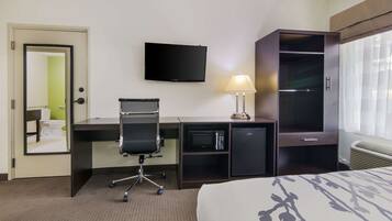 A hotel room with a bed, a desk with a chair, a television, a lamp, a wardrobe, and a microwave.