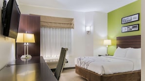 A hotel room with a bed, a desk, a TV, a lamp, and a window with curtains.