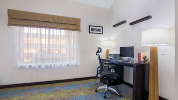 Habitación de hotel con escritorio, silla, dos lámparas, televisor y alfombra estampada.