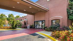 A brick building with a red brick entrance, a covered walkway, and a landscaped area with flowers and shrubs.