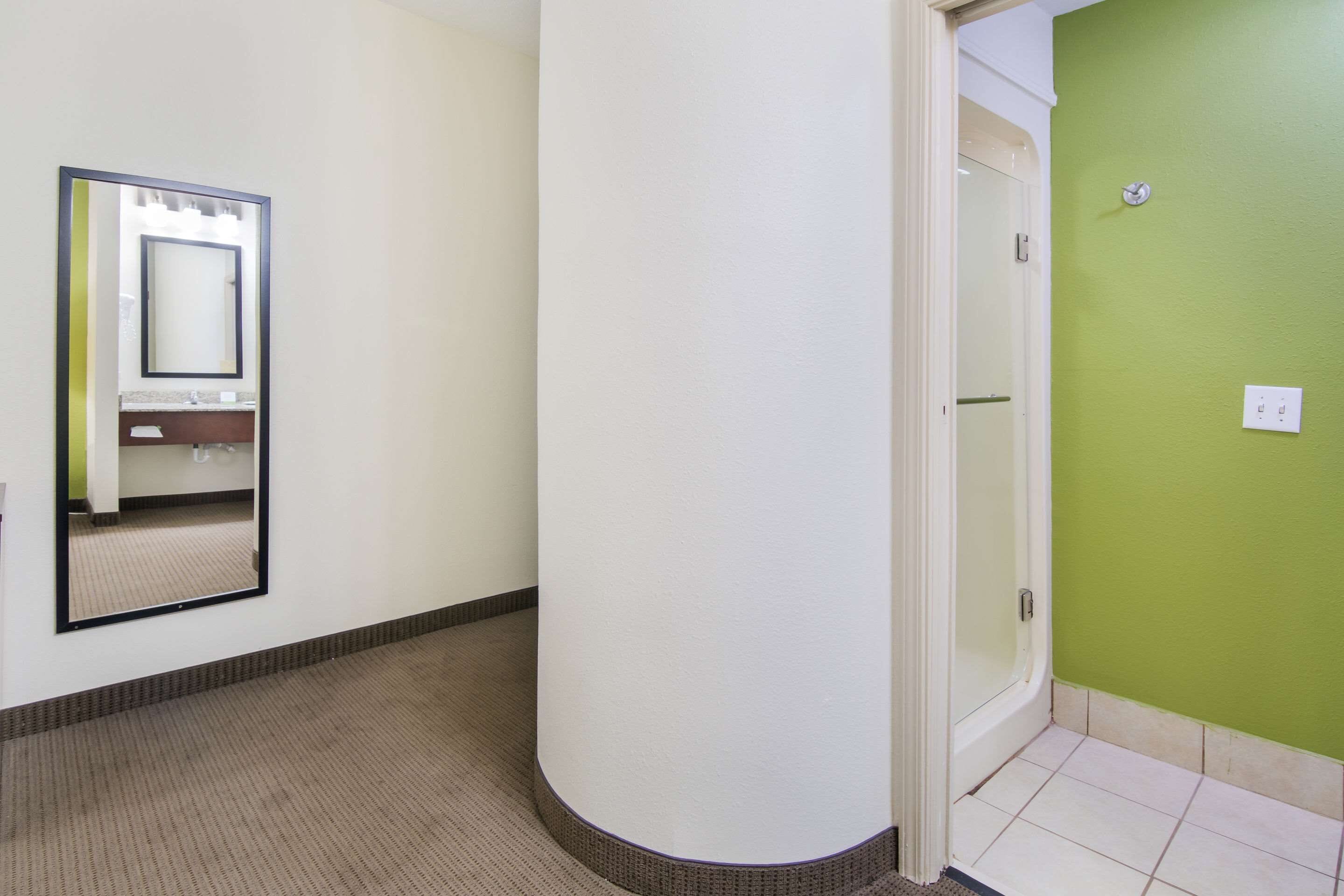 Un pasillo con un espejo, una puerta que da a un baño y una pared verde.