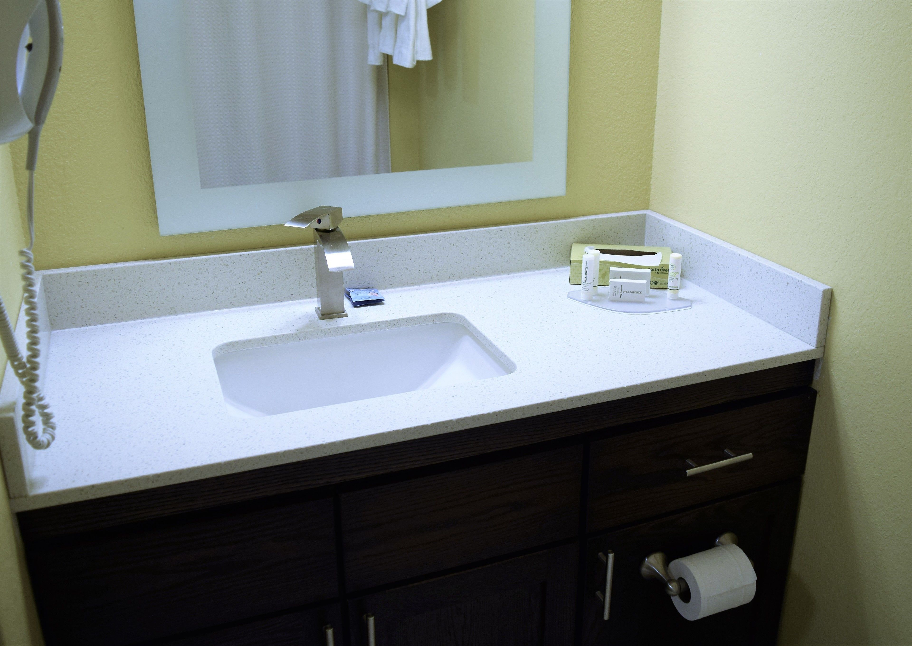 Un baño con un lavabo blanco, un espejo, un perchero para toallas y un porta papel higiénico.