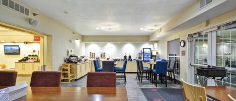 A hotel lobby with a reception desk, seating area, and a kitchenette.
