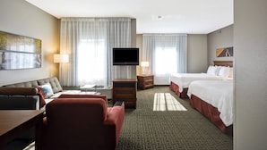 Habitación de hotel con sofá, dos camas, televisión, escritorio y lámpara.