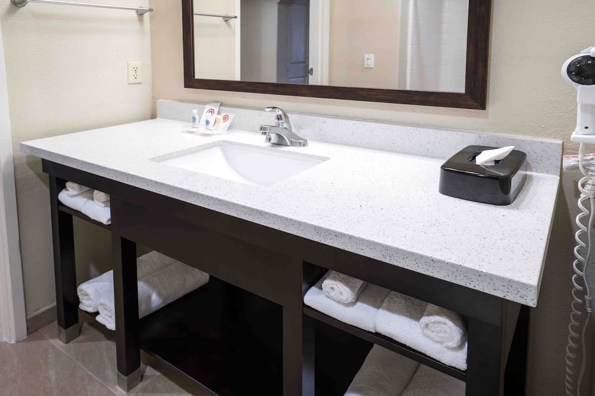 Un baño con lavamanos blanco, tocador de madera oscura, un espejo y un perchero para toallas.