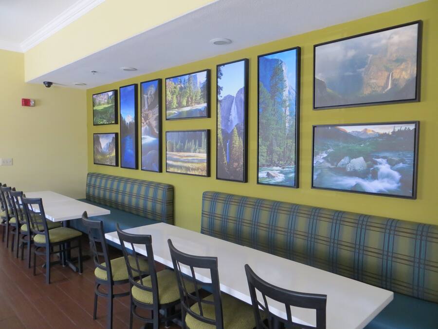 A dining area with multiple tables and benches, a ceiling fan, and a row of framed landscape pictures on the wall.