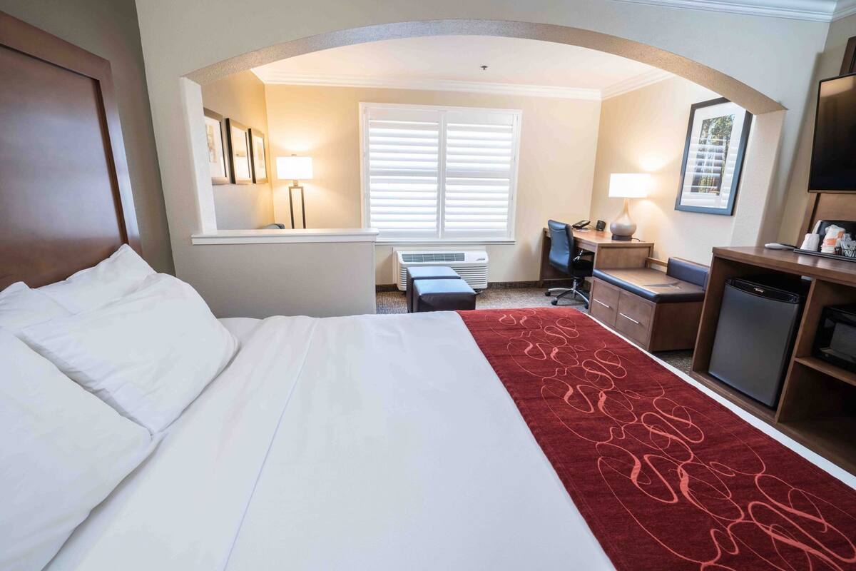 A hotel room with a bed, desk, chair, and a small kitchenette.
