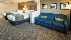 A hotel room with two beds, a blue sofa, and framed pictures on the wall.