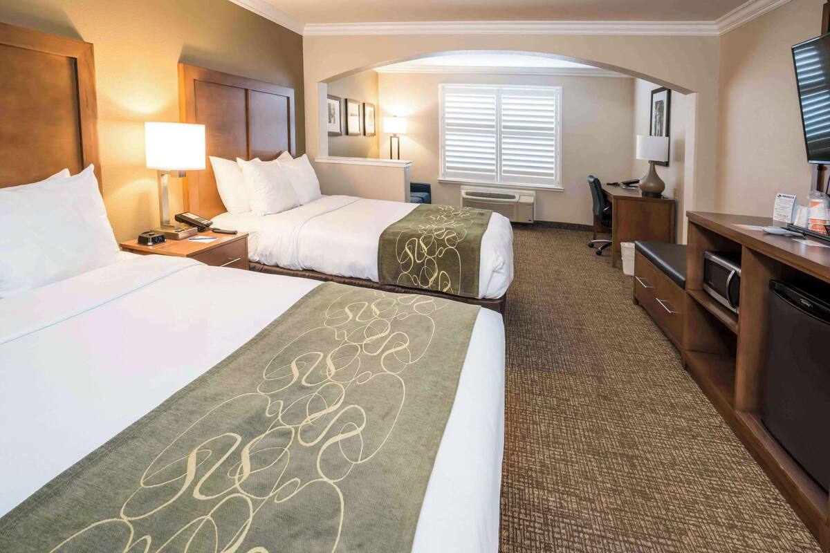 A hotel room with two beds, a desk, a television, and a window with blinds.