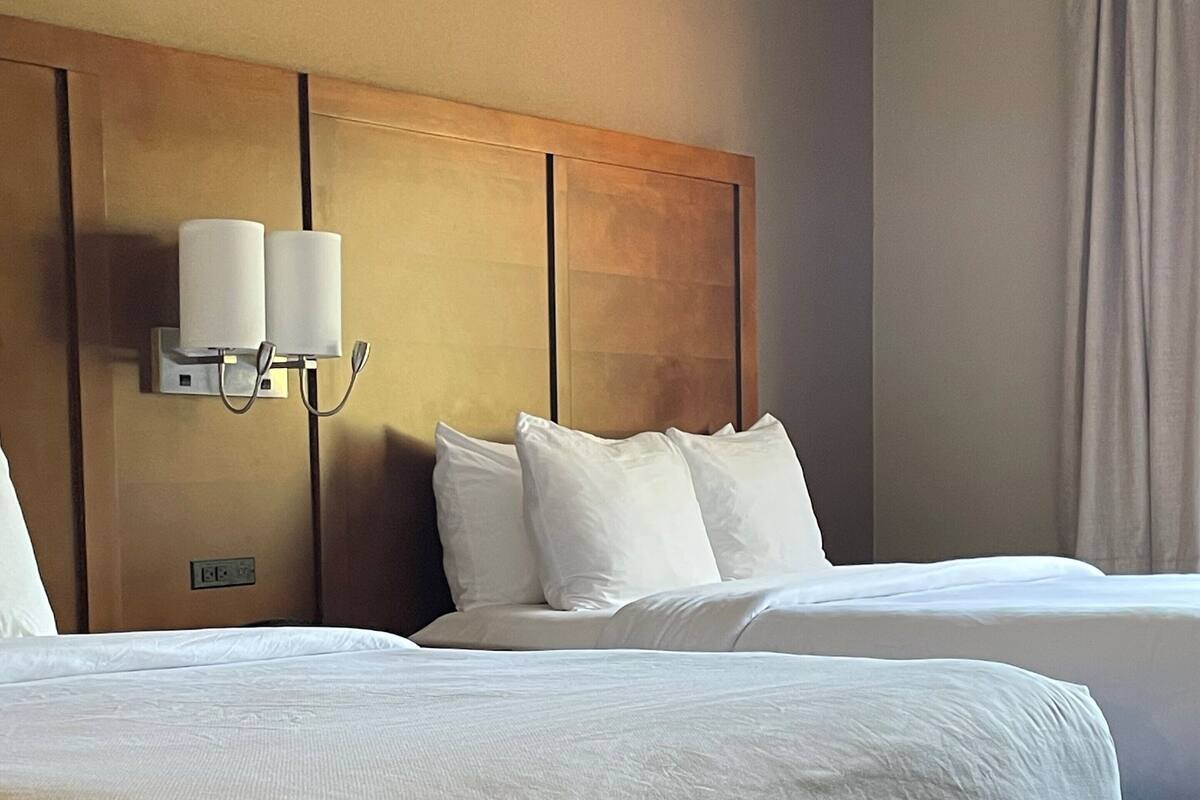 Habitación de hotel con dos camas, cabecera de madera y lámpara fijada a la pared.