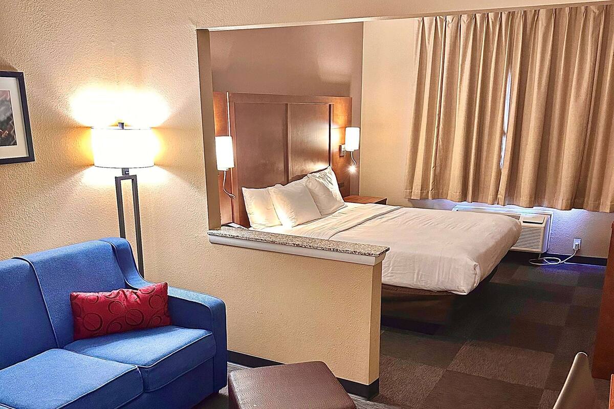 Habitación de hotel con cama, sofá azul, almohada roja, lámpara y televisor montado en la pared.