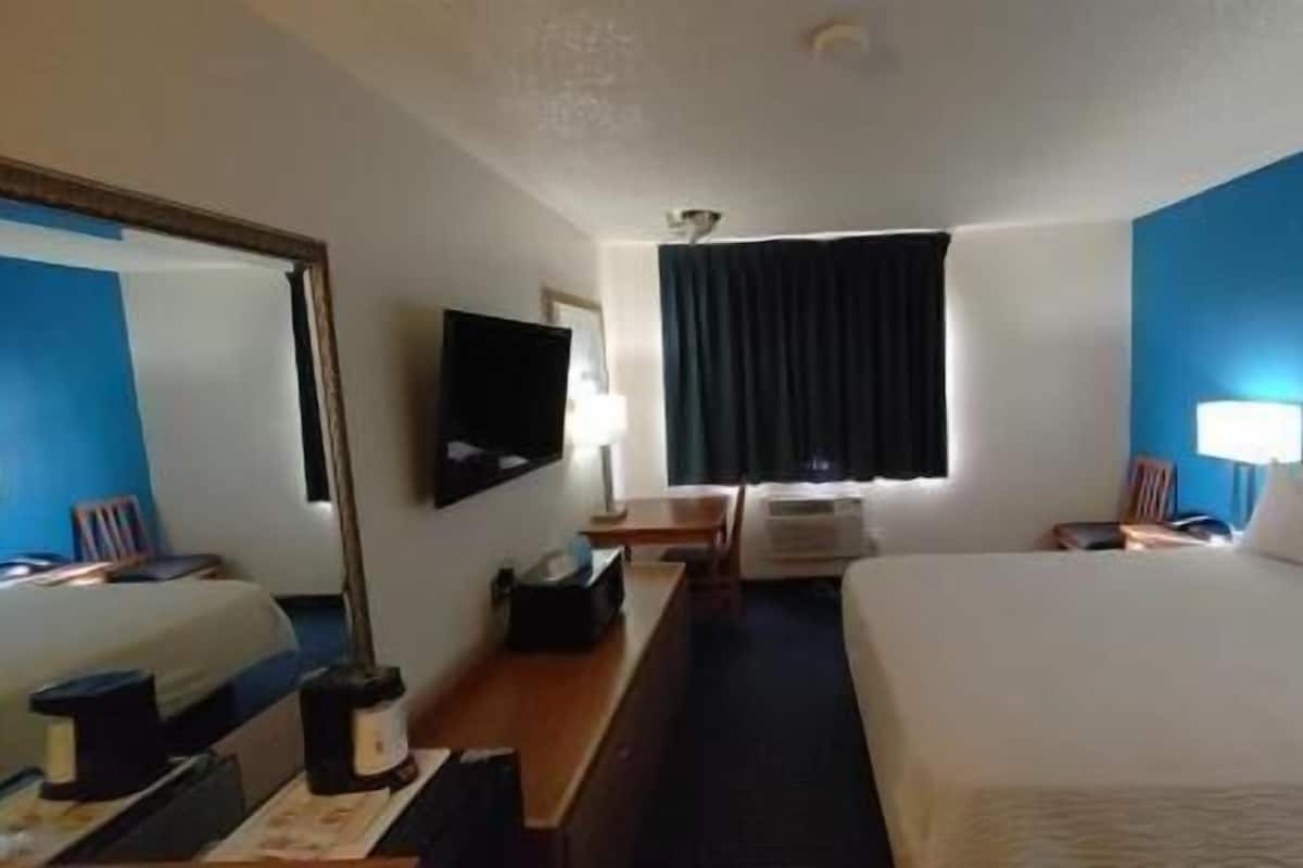 A hotel room with a bed, a desk, a chair, a television, and a window with curtains.