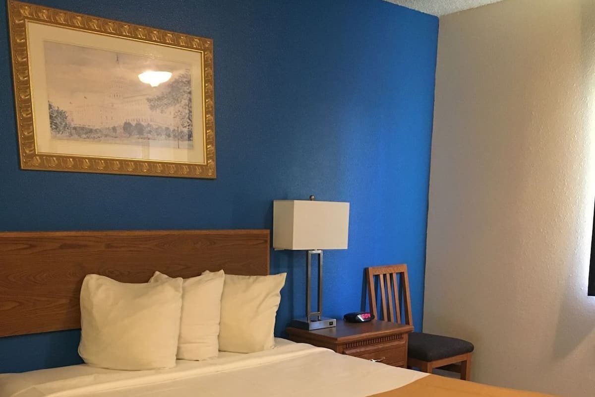A hotel room with a bed, a nightstand, a lamp, a framed picture on the wall, and a 'Hello Sunshine' sign on the bedspread.