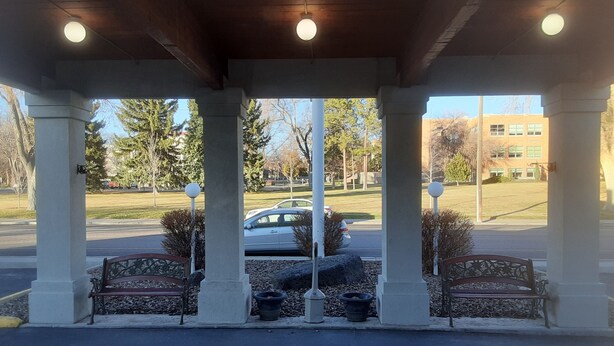 A covered outdoor area with benches, potted plants, and a view of a parking lot and buildings in the background. - Days Inn by Wyndham Pocatello University Area (Pocatello)