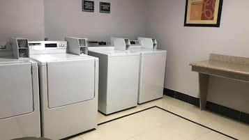 A laundry room with four white washing machines, a trash bin, and a granite countertop.