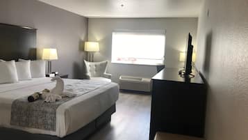 Una camera d'albergo con un letto, due lampade sui comodini, una scrivania con un computer, una finestra e un condizionatore d'aria a parete.