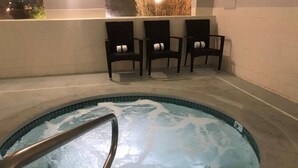 Un jacuzzi con escalera metálica, rodeado de sillas oscuras con cojines blancos.