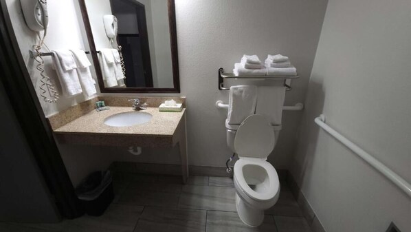 A compact hotel bathroom with a sink, toilet, and towel rack. - West Valley Inn (West Valley City)