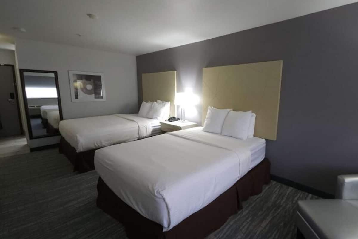 A hotel room with two beds, a desk, a chair, and a mirror.