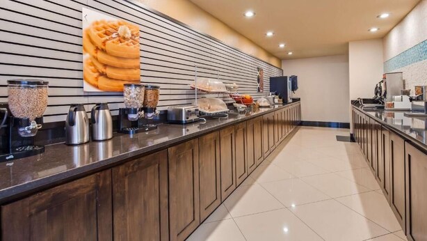 Una barra de desayuno con diversos alimentos y electrodomésticos, como una máquina para gofres, una cafetera y un tostador.