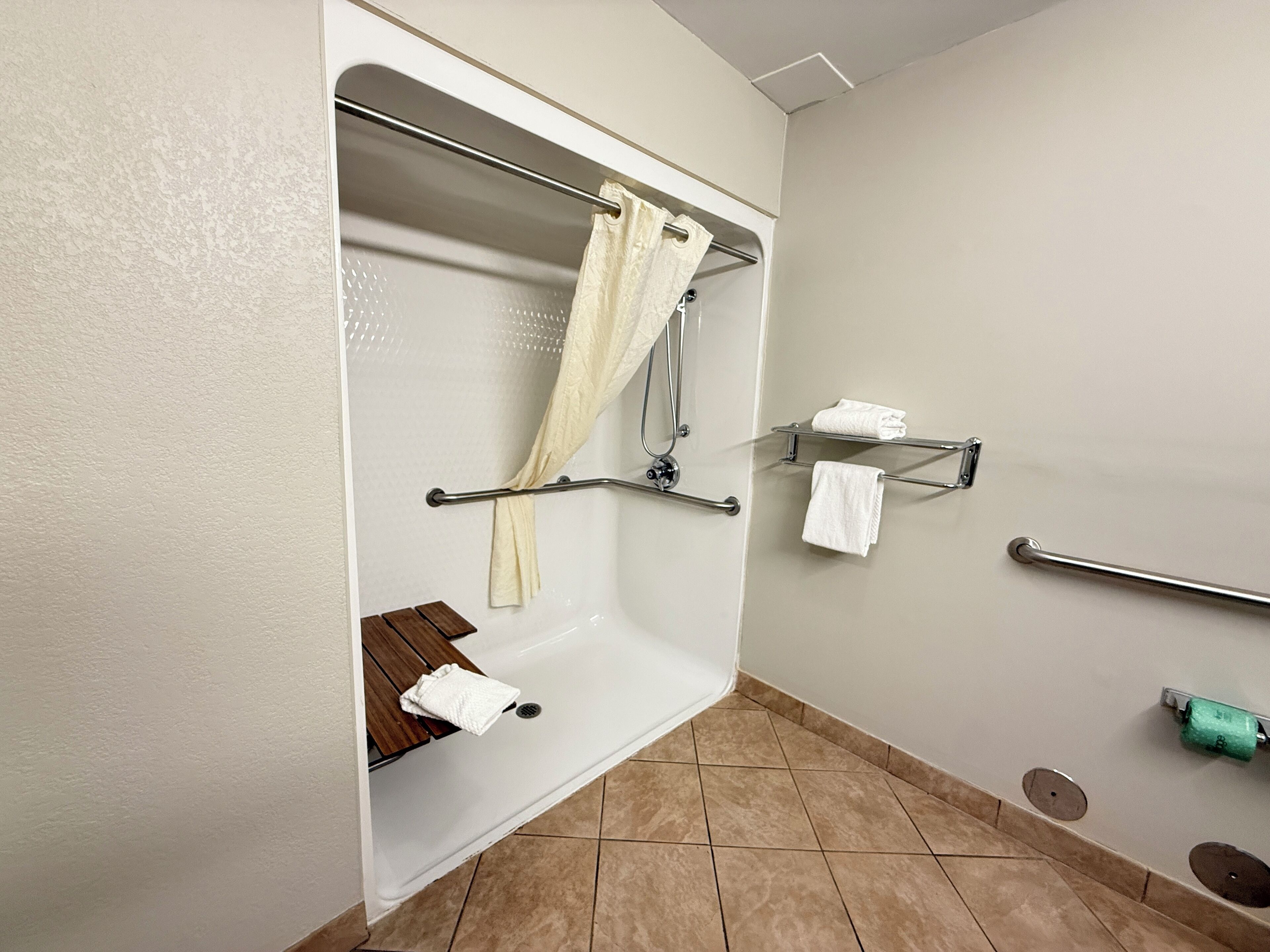 Une salle de bain équipée d’une douche, de barres d’appui, d’un banc et d’un porte-serviettes.