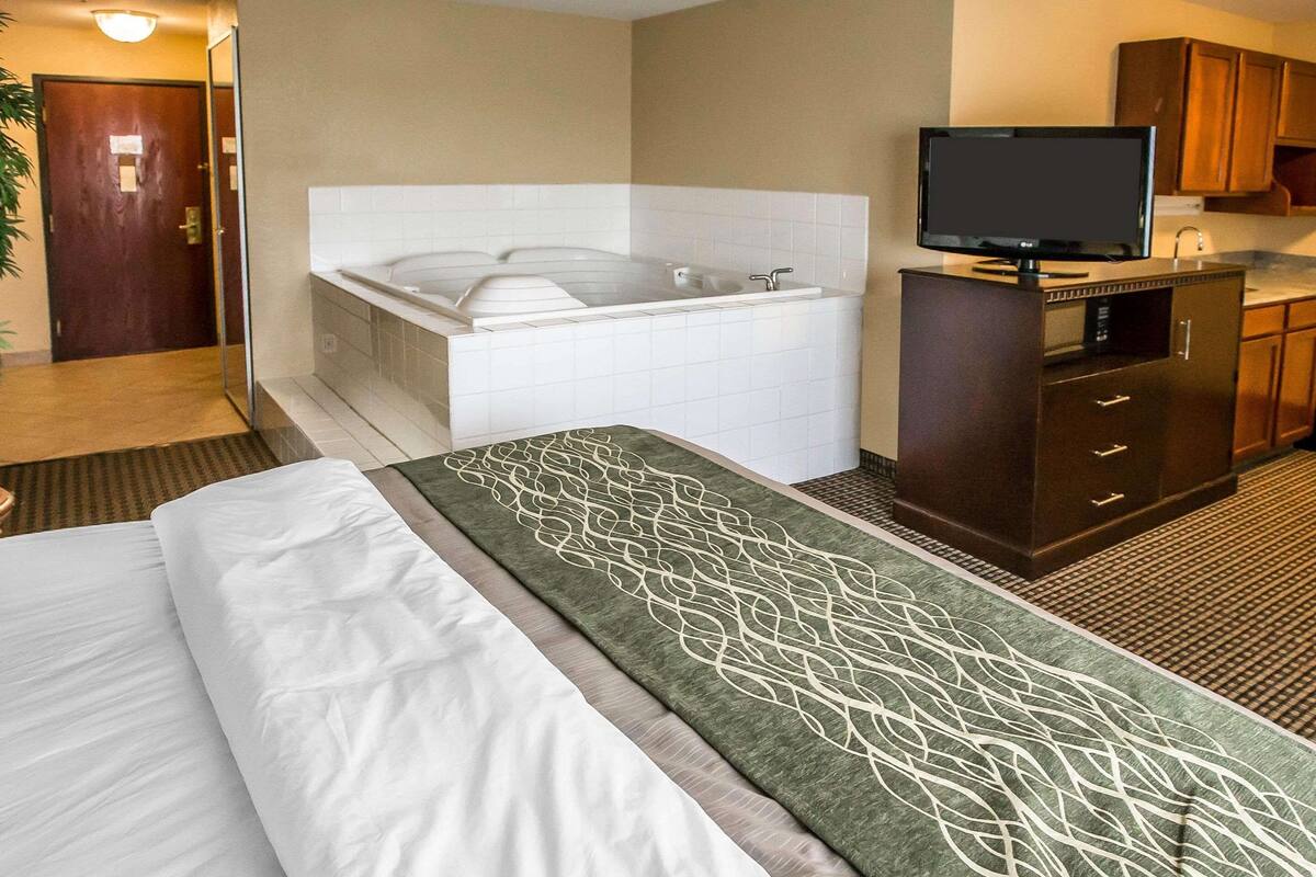 Habitación de hotel con cama, bañera grande, televisión y kitchenette.