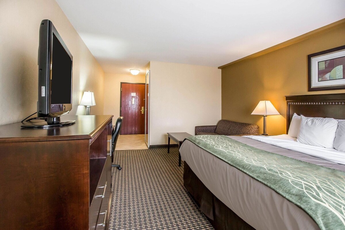 A hotel room with a bed, a desk, a chair, a television, and a door.