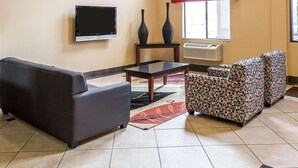 A living room with a sofa, armchairs, a coffee table, a flat-screen TV, two vases, and a window with a red curtain.