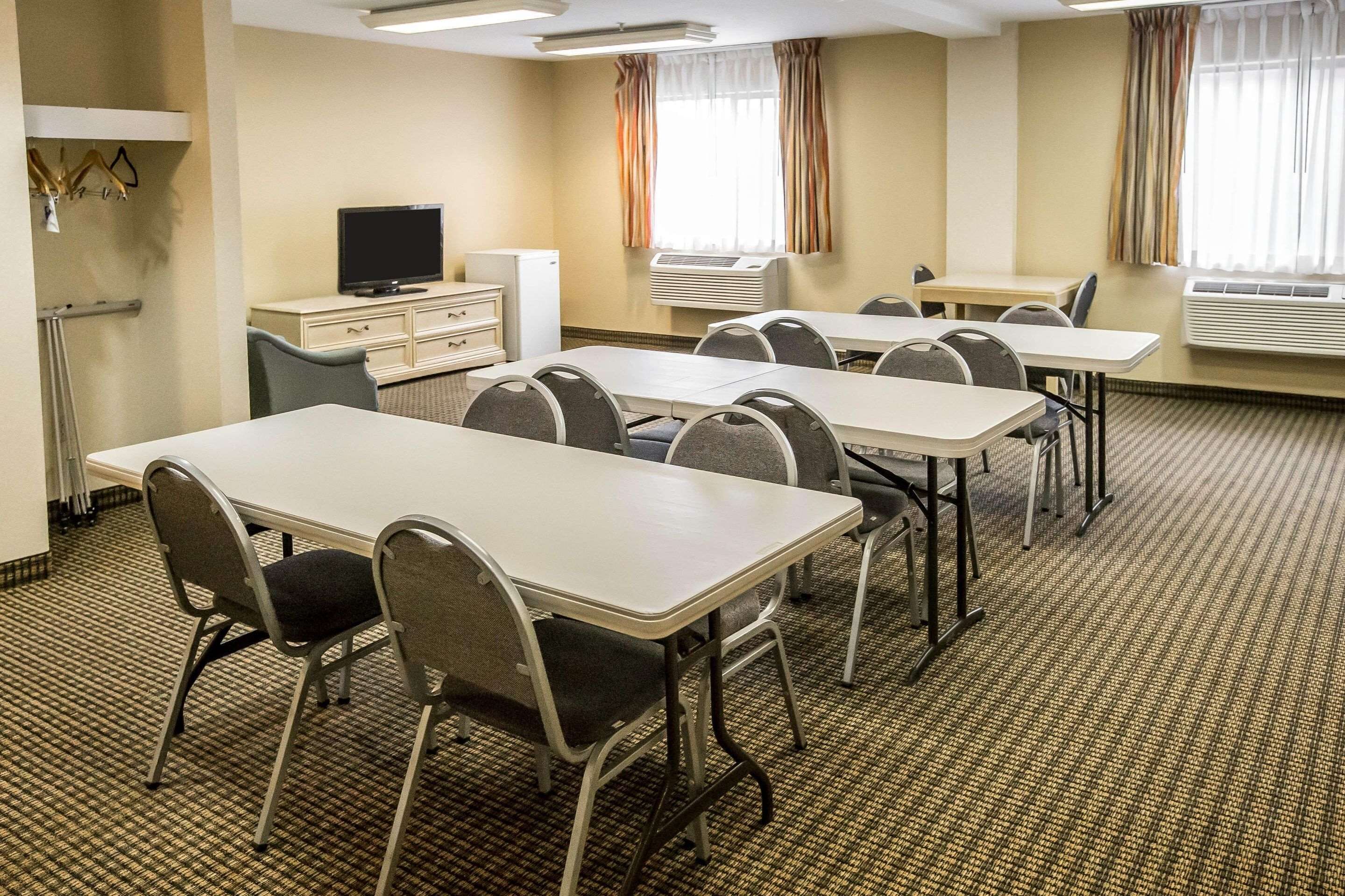 A hotel room with a conference table, chairs, a television, a mini-fridge, and an air conditioning unit.